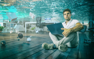 A man sitting in his flooded office, wishing he had a disaster recovery plan in place.