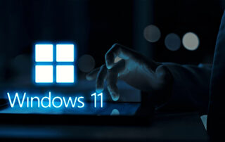 Hand interacting with a tablet displaying the Windows 11 logo in a dark, professional setting